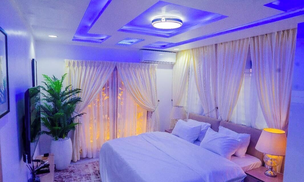 A bedroom with a bed, curtains, a potted plant, and a nightstand.