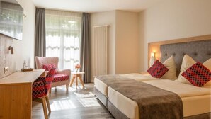 Une chambre d’hôtel avec un lit, un bureau, une chaise, une petite table avec un vase et un radiateur.