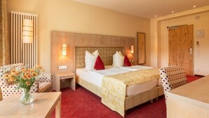 A hotel room with a bed, two bedside tables, a chair, a desk, and a vase with flowers. - Hotel Waldesrand (Herford)