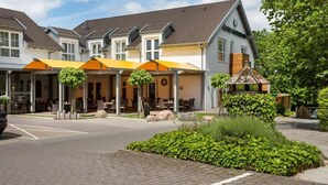 Une rangée de bâtiments blancs surmontés d’auvents orange, une rue pavée et de la verdure.
