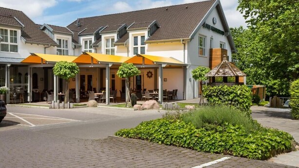 A row of white buildings with orange awnings, a paved street, and greenery. - Hotel Waldesrand (Herford)