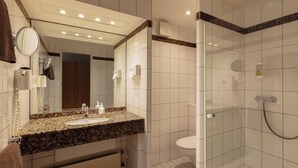 A bathroom with a granite countertop sink, a mirror, a toilet, and a glass-enclosed shower area. - Hotel Waldesrand (Herford)