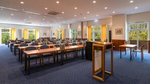 Une salle de conférence dotée de plusieurs tables et chaises, de grandes fenêtres donnant sur un espace verdoyant et d’un pupitre.