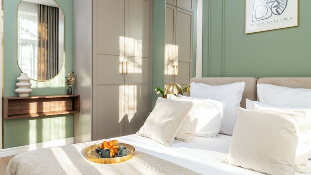 A neatly made bed with pillows and a tray of fruits and coffee cups, a large mirror, and a framed artwork on the wall. - Perfect Old Town Krakow's Architect Apartment AC WiFi King Size Bed Parking (Kraków)