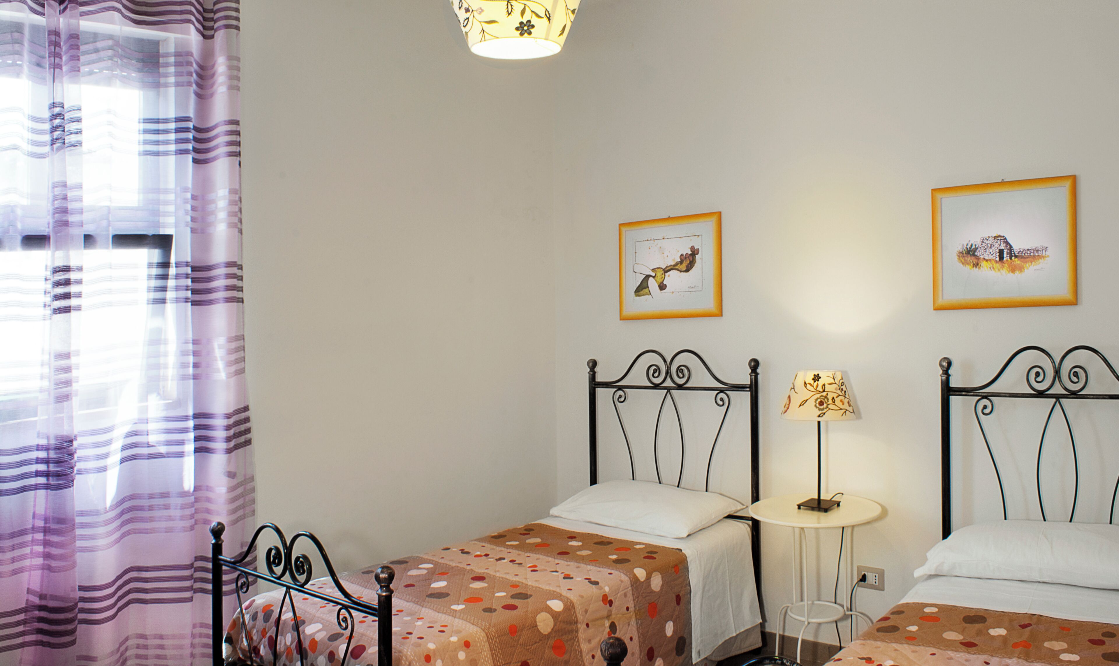 A bedroom with two single beds, a bedside table with a lamp, and two framed pictures on the wall.