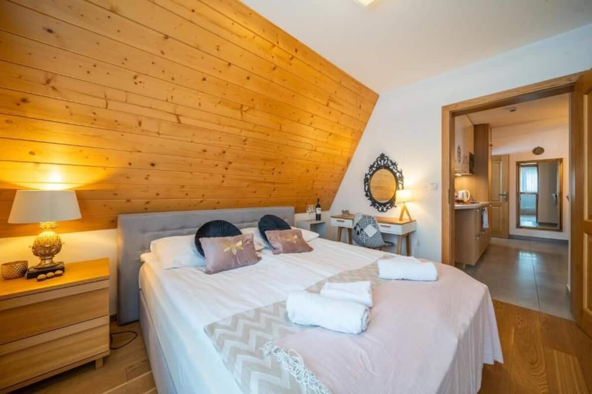 A bedroom with a wooden ceiling, a bed with pillows, a nightstand with a lamp, and a mirror.