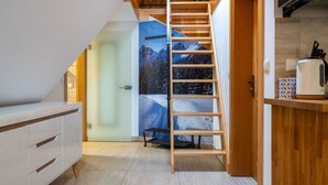 A narrow hallway with a wooden ladder leading to a door with a mountain view poster. - ANAapart (Zakopane)