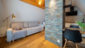 A modern living room with a sofa, a lamp, and a kitchen area with a stone wall. - ANAapart (Zakopane)