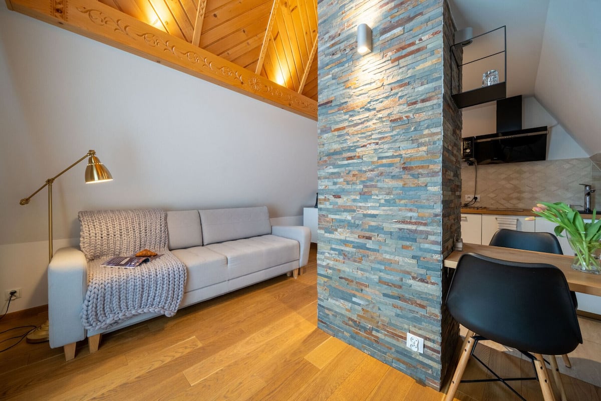 A modern living room with a sofa, a lamp, and a kitchen area with a stone wall.
