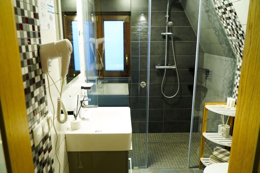 A bathroom with a glass-enclosed shower, a white sink, and a patterned tile wall.