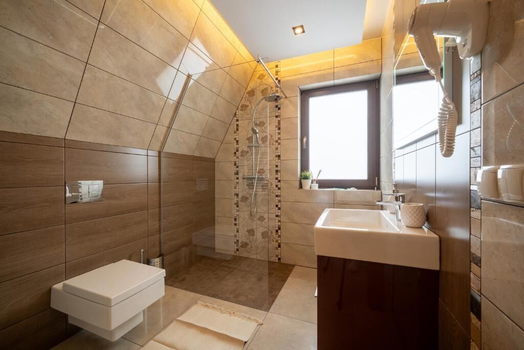 Et moderne badeværelse med bruser, toilet, håndvask og et vindue.