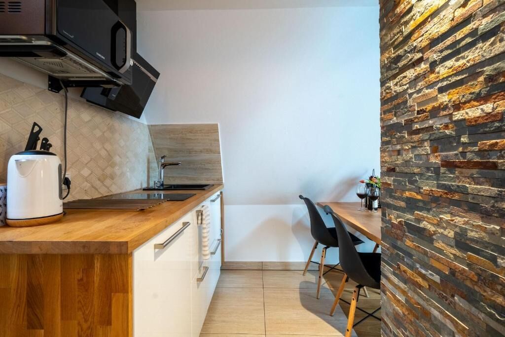 A compact kitchen with a wooden countertop, a kettle, a stove, and a stone wall.