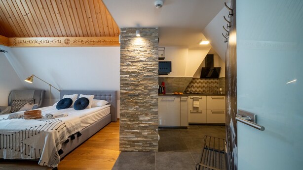 A bedroom with a bed, a desk, and a kitchen area with a stone wall. - ANAapart (Zakopane)