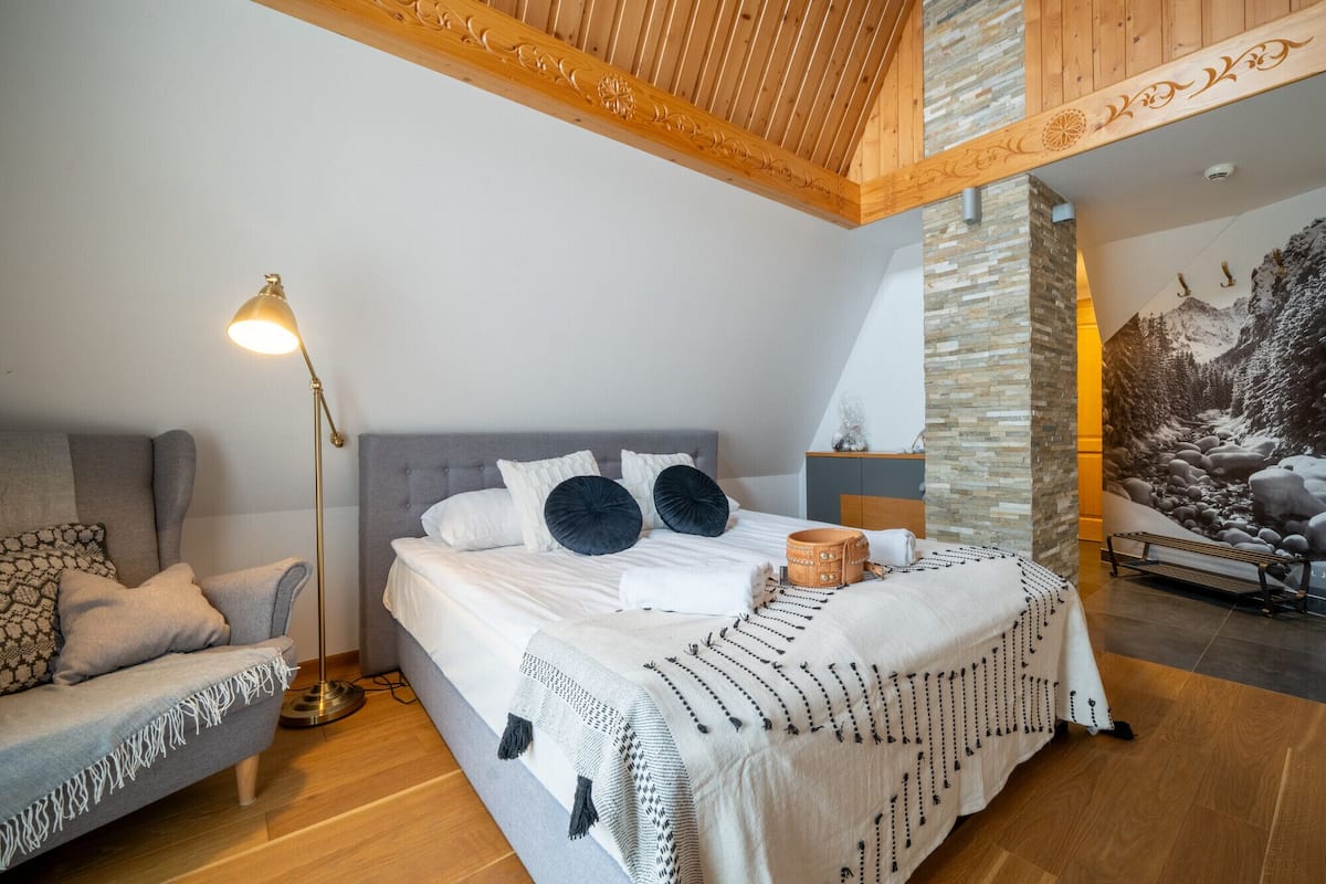 A bedroom with a bed, a sofa, a lamp, and a stone wall.