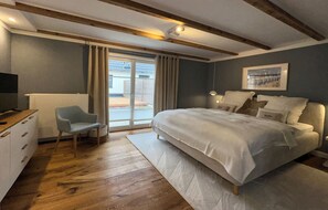 A bedroom with a bed, a chair, a desk, a radiator, and a window with curtains.