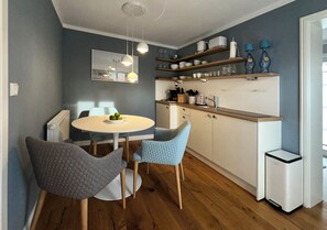 A modern kitchen with wooden cabinets, a white countertop, and a dining area with a round table and chairs.