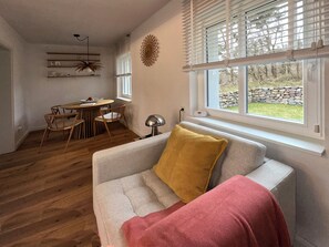 A living room with a sofa, a dining table with chairs, a decorative wall piece, and a window with blinds.