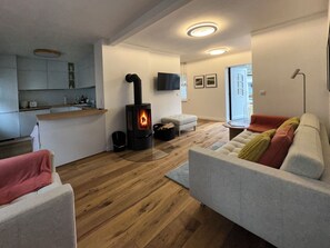 A modern living room with a fireplace, a sofa, a coffee table, and a kitchen area with a countertop and cabinets.