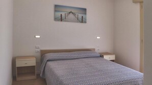 A bedroom with a bed, a nightstand, a wall-mounted air conditioner, and a painting of a pier. - Cozy Apartment With two Terraces (Lignano Sabbiadoro)