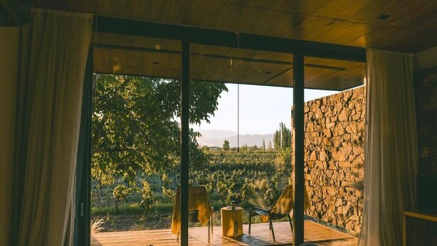 Una habitación con amplias ventanas, una pared de piedra y vistas a un viñedo.