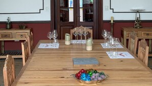 Un comedor con una mesa de madera dispuesta para una comida, flanqueada por sillas de madera, un candelabro e impresiones botánicas enmarcadas en las paredes.