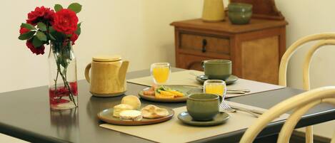 A dining table with breakfast items, a vase with flowers, and a wooden cabinet in the background.