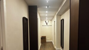En gang med trægulv, hvide vægge og et skilt der viser 'VATICAN BOUTIQUE ROOMS'.