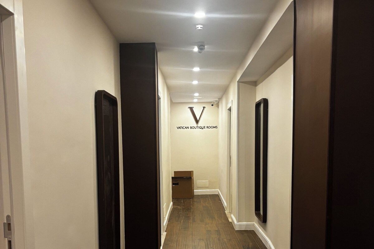 Un pasillo con suelo de madera, paredes blancas y un letrero que dice 'VATICAN BOUTIQUE ROOMS'.