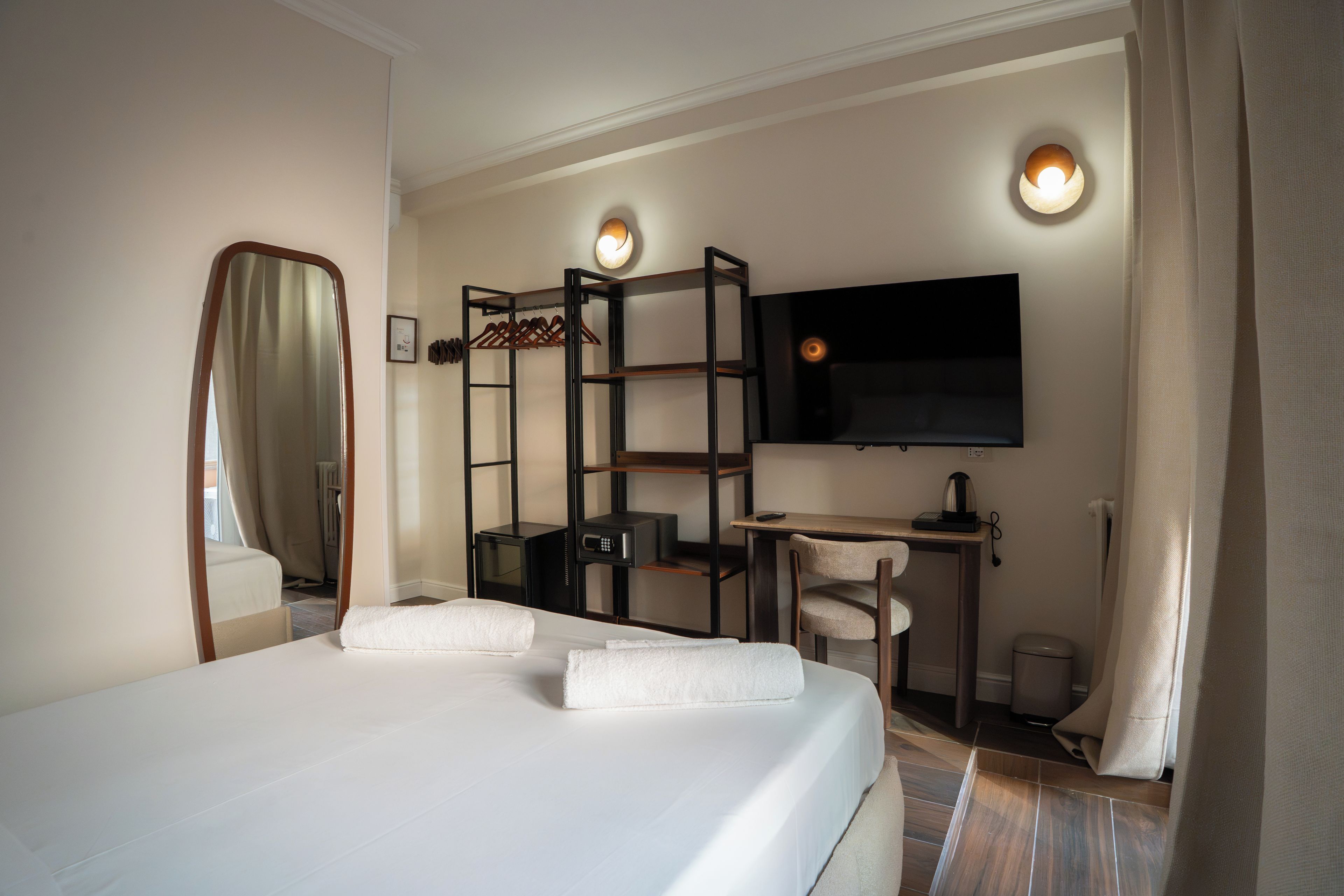 Una camera d'albergo con un letto, una scrivania, una sedia, una televisione e uno specchio.