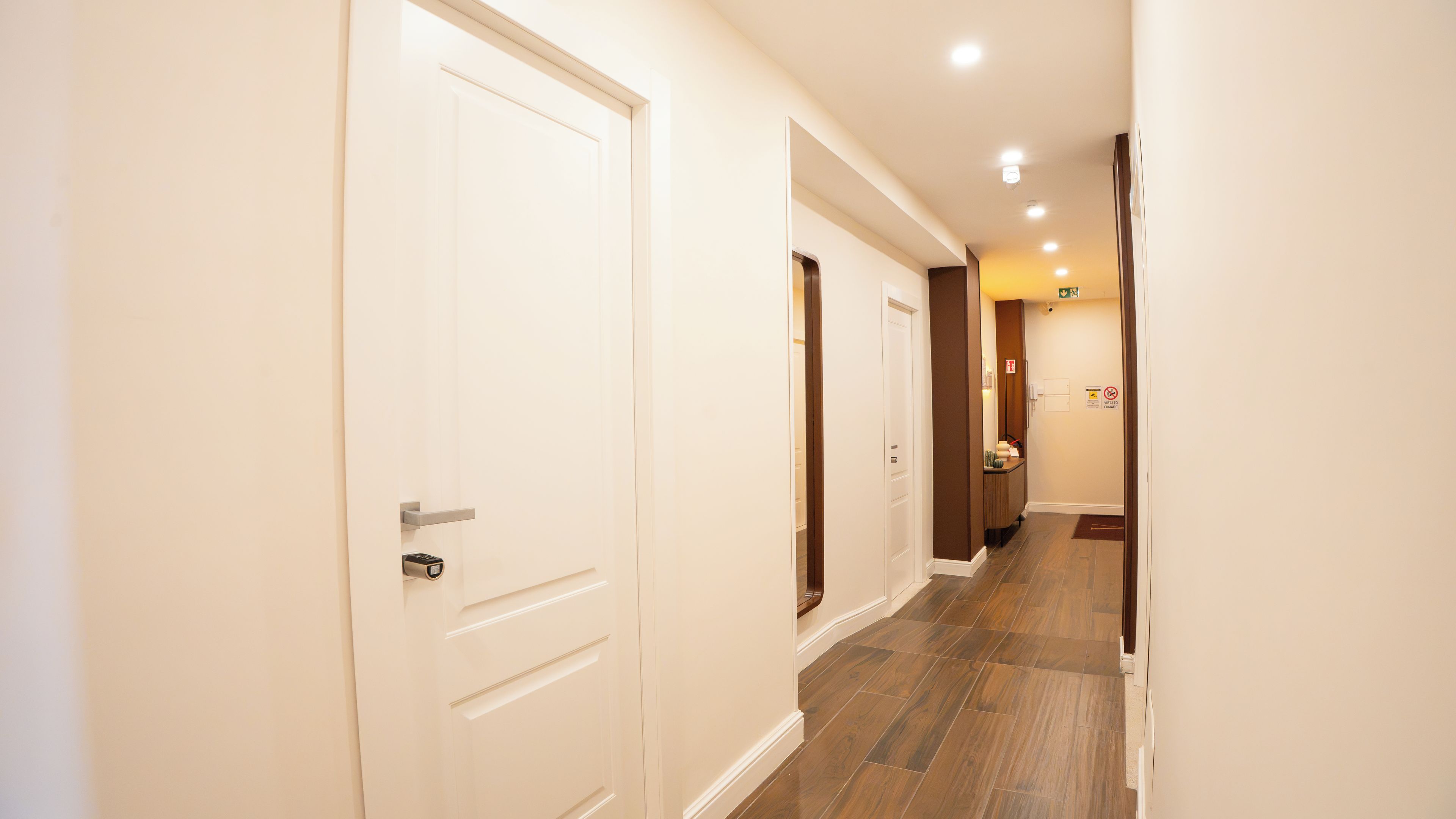 A hotel hallway with white doors, wooden flooring, and recessed ceiling lights.