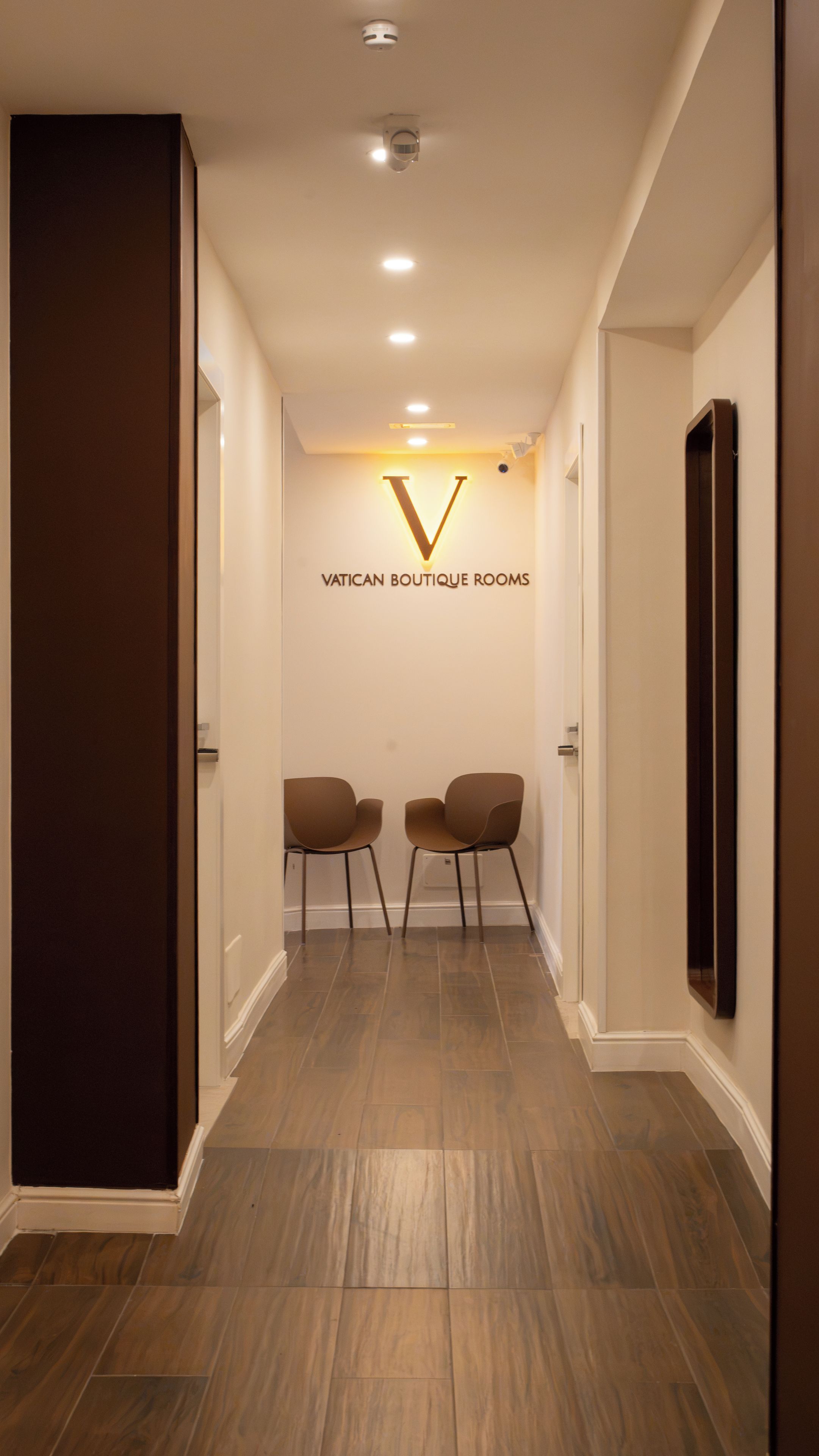 A hallway with a sign reading 'VATICAN BOUTIQUE ROOMS' and two chairs facing each other.