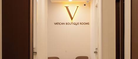 Un pasillo con un cartel que dice 'VATICAN BOUTIQUE ROOMS' y dos sillones enfrentados.