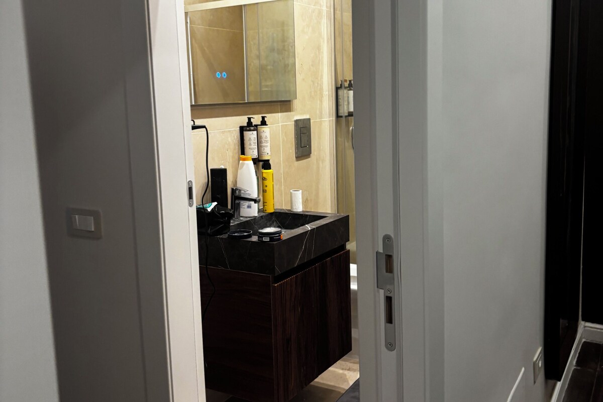 Un baño moderno con un tocador oscuro, un espejo grande y una zona de ducha.