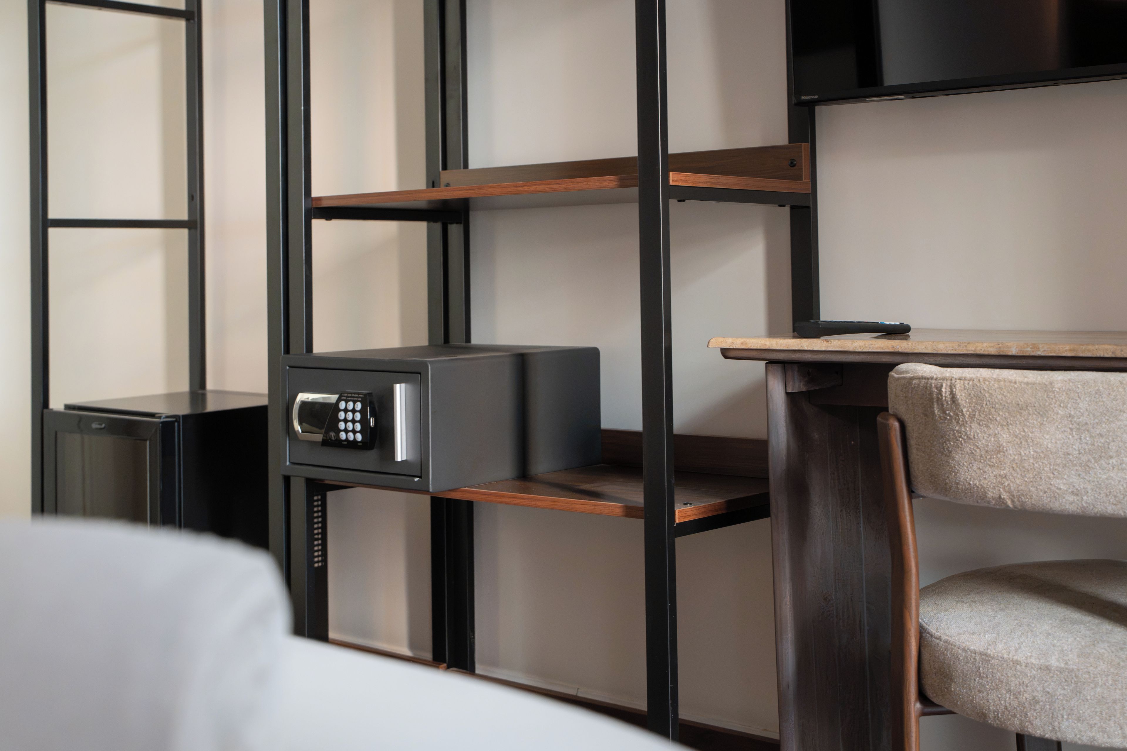 A hotel room with a bed, a desk with a chair, a TV, and a safe.
