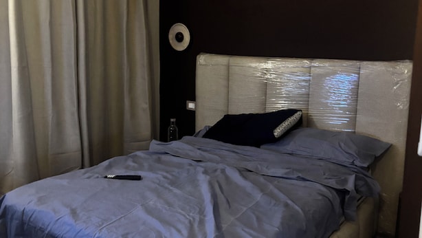 Et soveværelse med seng, gardiner, vægur og et sengebord.