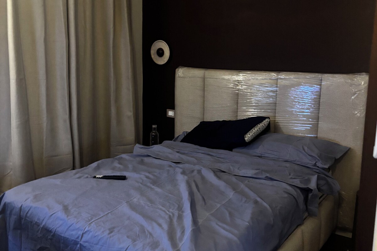 Un dormitorio con cama, cortinas, un reloj de pared y una mesita de noche.