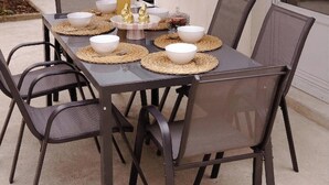 Un espace extérieur aménagé pour les repas, avec une table dressée pour quatre personnes, entourée de chaises, et une terrasse couverte.