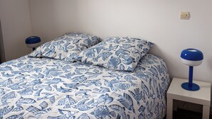 Un lit avec une literie à motifs, une table de chevet avec une lampe et un interrupteur mural.