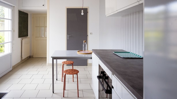 Une cuisine moderne avec un sol carrelé de couleur blanche, un plan de travail foncé et deux tabourets.