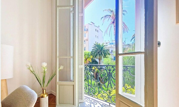 Ein Zimmer mit Blick auf einen Balkon, einer Vase mit Blumen und einem Sessel.