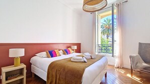 A hotel room with a bed, bedside table, lamp, and a view of the outdoors. - N&J - CLOS DES FLEURS - Luminous - Spacious (Nice)