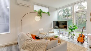 Een moderne woonkamer met een bank, stoelen, een televisie en een gitaar.