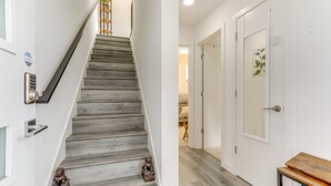 Een trap met een houten afwerking, een deur met een planten decoratie en een klein tafeltje met een houten blad.