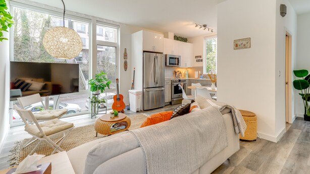Een moderne woonkamer met een bank, een televisie en een eethoek met een tafel en stoelen.