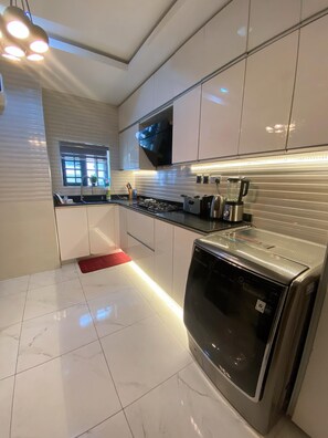 A modern kitchen with white cabinets, a built-in oven, and a window with blinds. - L Rina Apartment (Lekki)