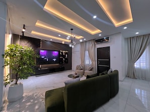 A modern living room with a flat-screen TV, a green sofa, a coffee table, and a potted plant. - L Rina Apartment (Lekki)