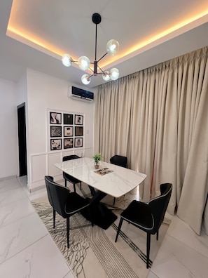 A dining area with a marble table, black chairs, a chandelier, and a large window with curtains. - L Rina Apartment (Lekki)