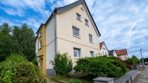 A multi-story residential building with a sloped roof, surrounded by greenery and a paved pathway. - Apartment 'Beautiful 100m² Holiday' with Private Terrace, Shared Garden and Wi-Fi (Herford)