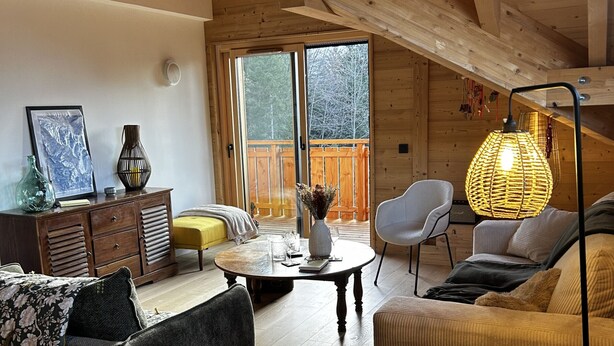 Un accogliente soggiorno con soffitto in legno, un tavolo da pranzo con sedie, un divano e un'ampia finestra.