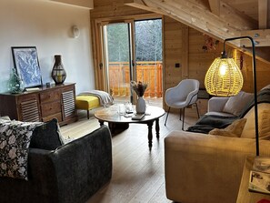 A cozy living room with a wooden ceiling, a dining table with chairs, a sofa, and a large window. - Modern apartment with parking - 8 guests (Arâches-la-Frasse)